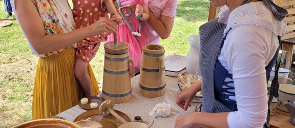 1 Mitarbeiterin des Agroneum macht den Workshop Buttern mit 2 Frauen und 2 kleinen Mädchen.