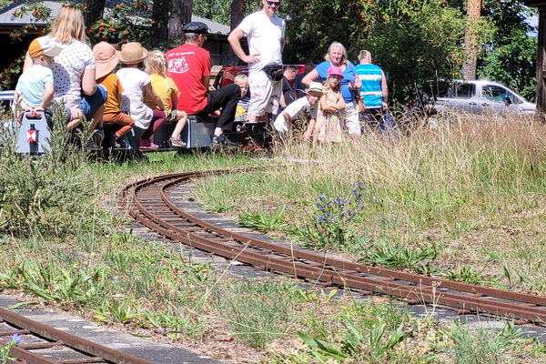 Lokführer und mehrere Kinder sitzen auf einer Modelleisenbahn im Agroneum.
