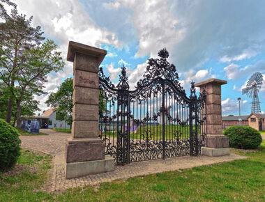 Großes, schwarz verzinktes Eingangstor zwischen 2 Steinpfeilern