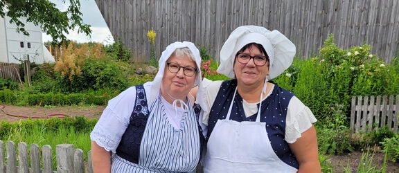 Zwei Mitarbeiterinnen des Agroneum, bekleidet mit einer Tracht stehen nebeneinander im Museumsgarten.