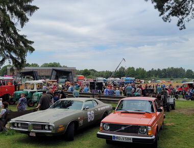 im Vordergrund zwei Oldtimer Autos, im Hintergrund viele Besucher des Agroneum