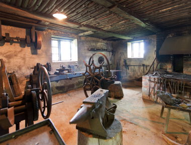 in der Mitte ein Amboss, daneben weitere Geräte und Werkzeuge einer Schmiede