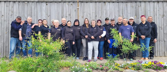 19 Mitarbeiterinnen und Mitarbeiter des Agroneums stehen nebeneinander vor einer Holzwand